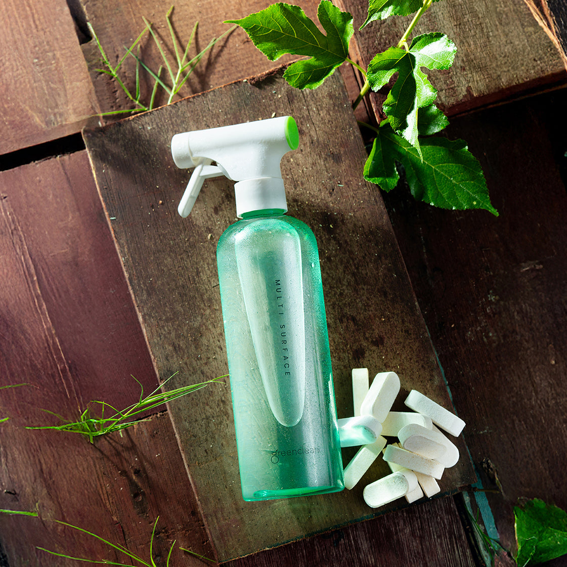 Greencleani eco-friendly multi-surface cleaner in a green reusable spray bottle, shown with cleaning tablets and green leaves on a wooden surface. A safe, non-toxic cleaning solution for Malaysian homes