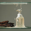 Greencleani eco-friendly handsoap in an elegant frosted white smoke glass dispenser bottle, held gently in hands with a leafy green background. A non-toxic, gentle hand soap for Malaysian families